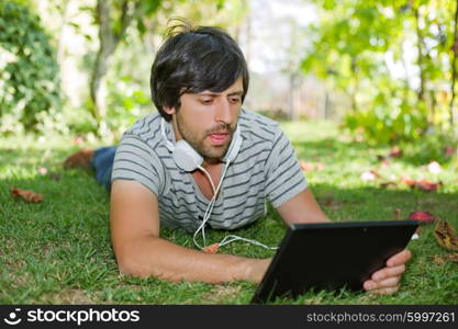 young man relaxing with a tablet pc listening music with headphones on a the park, outdoor