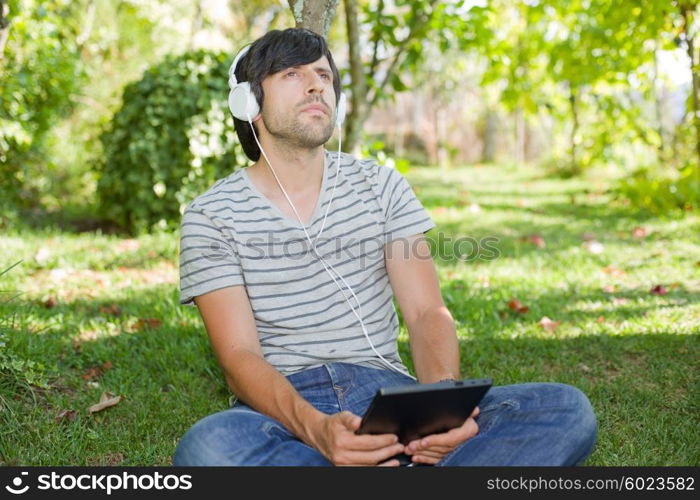 young man relaxing with a tablet pc listening music with headphones on a the park, outdoor