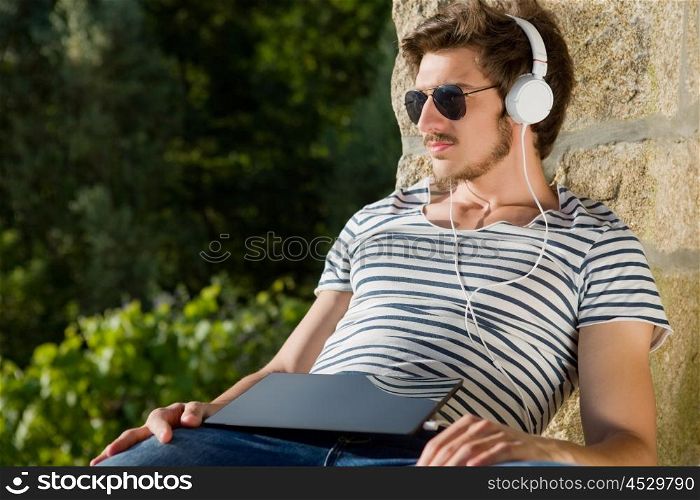 young man relaxing with a tablet pc listening music with headphones, outdoor