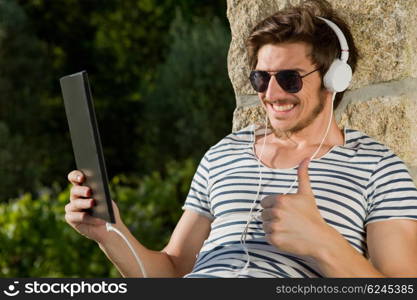 young man relaxing with a tablet pc listening music with headphones, outdoor