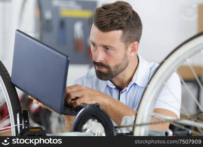 young man repairing bicycle with the help of a laptop