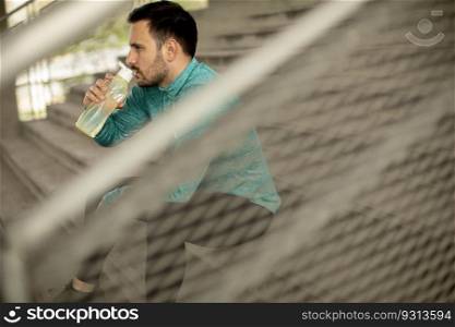 Young man resting during training with bottle of water in urban environment