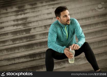Young man resting during training with bottle of water in urban environment