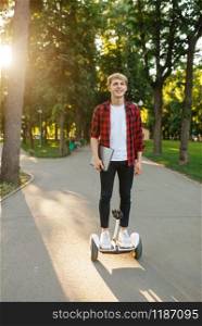 Young man riding on mini gyro board in summer park. Outdoor recreation with electric gyroboard. Eco transport with balance technology, electrical gyroscope vehicle