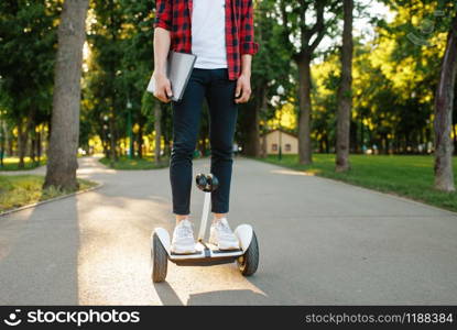 Young man riding on mini gyro board in summer park. Outdoor recreation with electric gyroboard. Eco transport with balance technology, electrical gyroscope vehicle. Young man riding on mini gyroboard in summer park