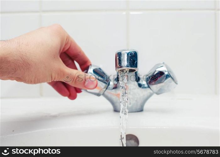 Young man&rsquo;s hand is turning a tap in a bathroom