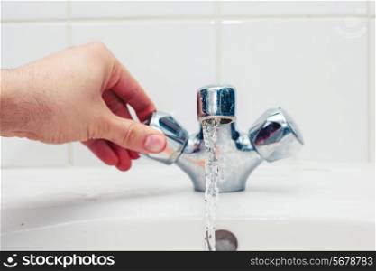 Young man&rsquo;s hand is turning a tap in a bathroom
