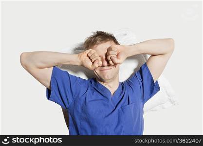 Young man rubbing eyes while waking up over colored background