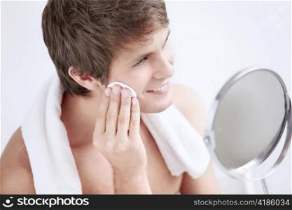 Young man rubbing lotion face in the mirror
