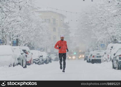 Young man runner under a snowfall in the city