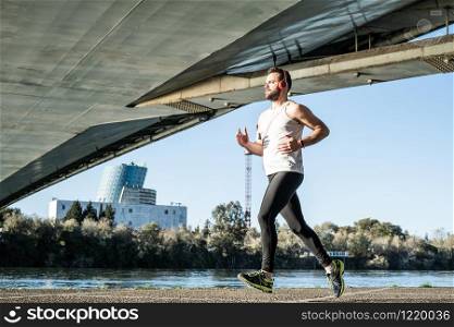 young man running in a white shirt across a bridge. He?s listening to music and he?s got some helmets on.