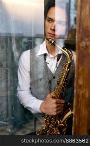 Young man saxophonist with instrument view from window. Cozy home interior. Soft focus.. Young man saxophonist with instrument view from window