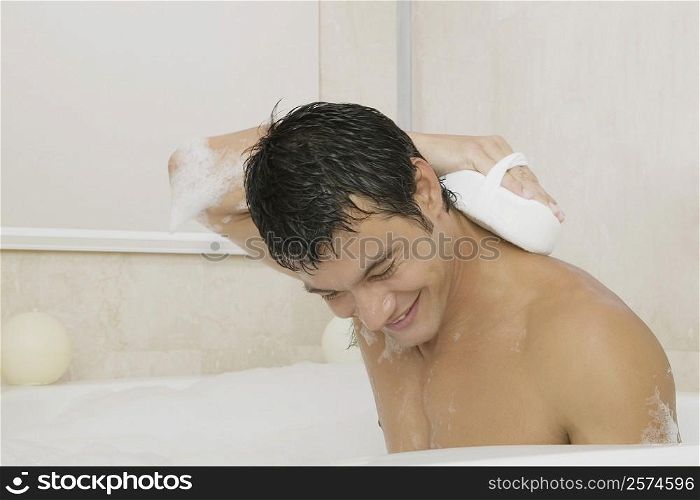 Young man scrubbing his back with a loofah in the bathtub