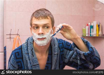 Young man shaves the stubble on his cheek