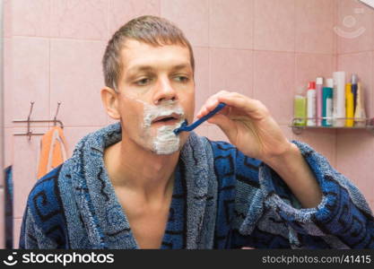 Young man shaving in front of mirro