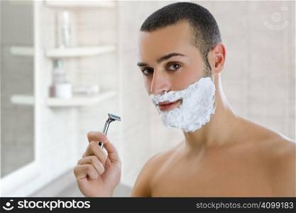 Young man shaving indoors. Copy space