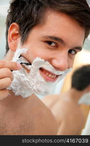 young man shaving with razor and shaving cream in the bathroom