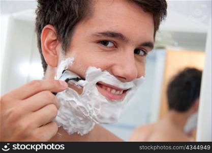 young man shaving with razor and shaving cream in the bathroom