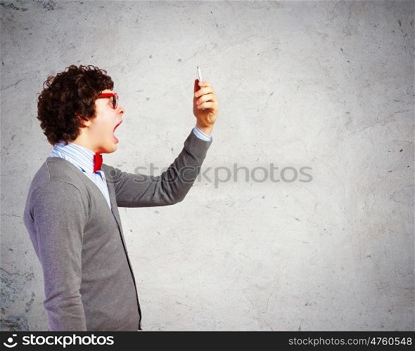 Young man shouting at his mobile phone. Young businessman with a red tie shouting furiously at his mobile phone