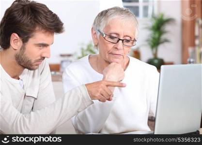 Young man showing a senior woman how to use a laptop