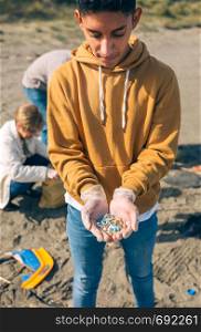 Young man showing microplastics collected on the beach. Young man showing microplastics