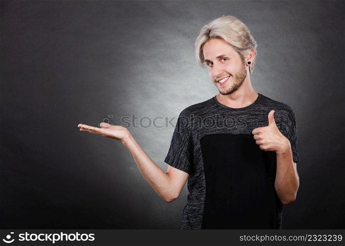 Young man showing presenting. Stylish content guy holding empty hand palm copy space for product making thumb up gesture. Advertising concept.. Guy holding empty hand palm copy space for product