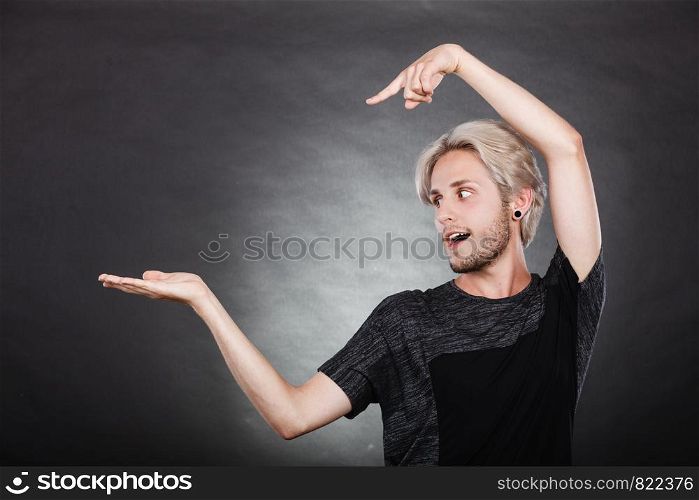Young man showing presenting. Stylish guy pointion with finger, holding empty hand palm copyspace for product. Fashion, advertising concept. Studio shot on dark. Guy holding empty hand copy space for product