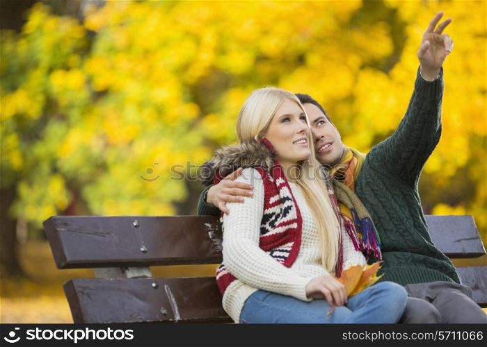 Young man showing something to woman while gesturing in park during autumn