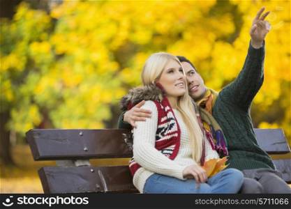 Young man showing something to woman while gesturing in park during autumn