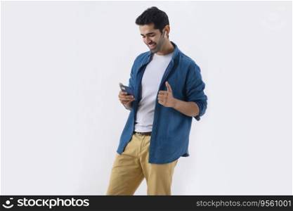 Young man showing thumb while listening music using earbuds and mobile