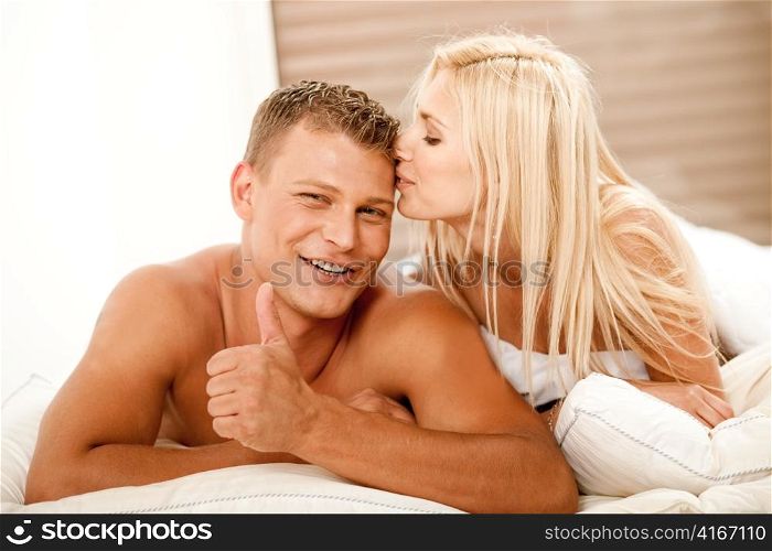 Young man showing thumbs up as woman kisses him on head
