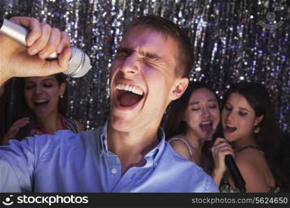 Young man singing into a microphone at karaoke, friends singing in the background