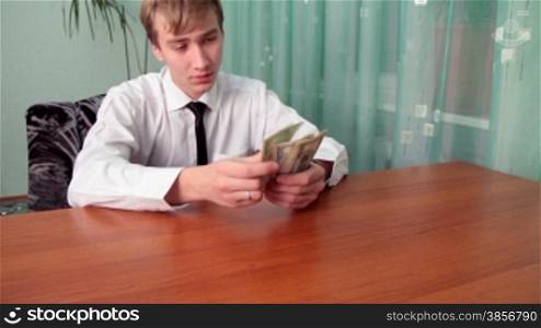 young man sits at a table at office and divides money.