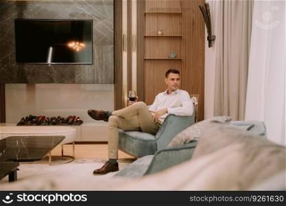 Young man sits in a luxury apartment, drinking red wine and and relaxing