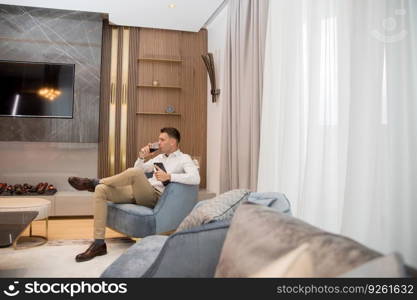 Young man sits in a luxury apartment, drinking red wine and holding a digital tablet