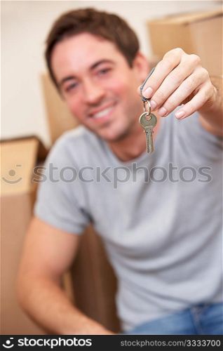 Young man sits on the floor around boxes holding a key in his hand