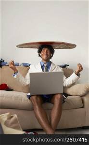 Young man sitting and using a laptop with a surfboard on his head