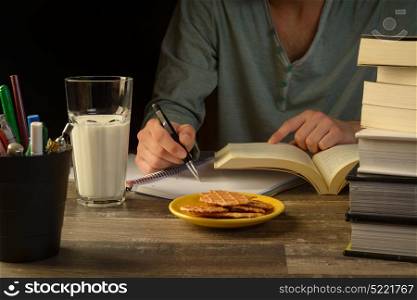 young man sitting at a study table desk with books a open sketch book and pencil bucket, university study, school.