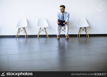 Young man sitting at chair in the waiting room with a folder in hand before an interview
