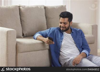 Young man sitting at home and looking at his phone. 