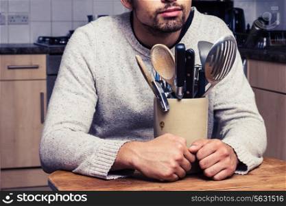 Young man sitting at table with kitchen utensils