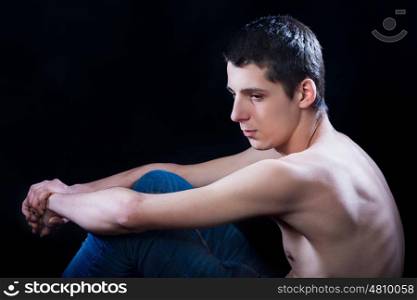 young man sitting down depressed against black