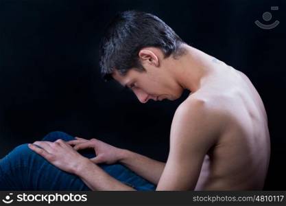 young man sitting down depressed against black
