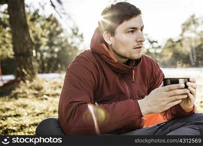 Young man sitting drinking coffee at lakeside