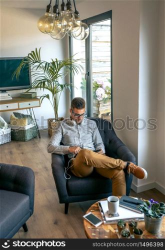Young man sitting in an armchair with tablet and headphones. Man sitting in an armchair with tablet