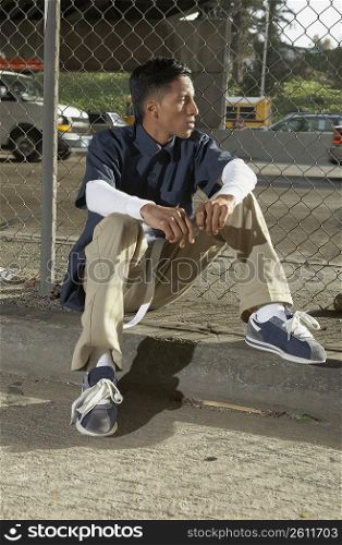 Young man sitting in front of a chain-link fence