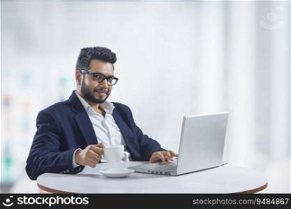 Young man sitting in his office while working on the laptop while drinking coffee. 