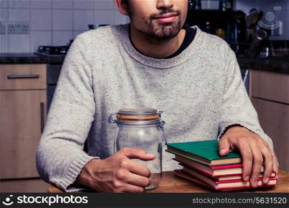 Young man sitting in kitchen with an empty jar and books