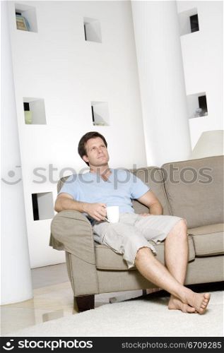 Young man sitting on a couch and holding a coffee cup