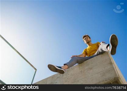 Young man sitting on a ledge looking around. Man sitting on a ledge looking around